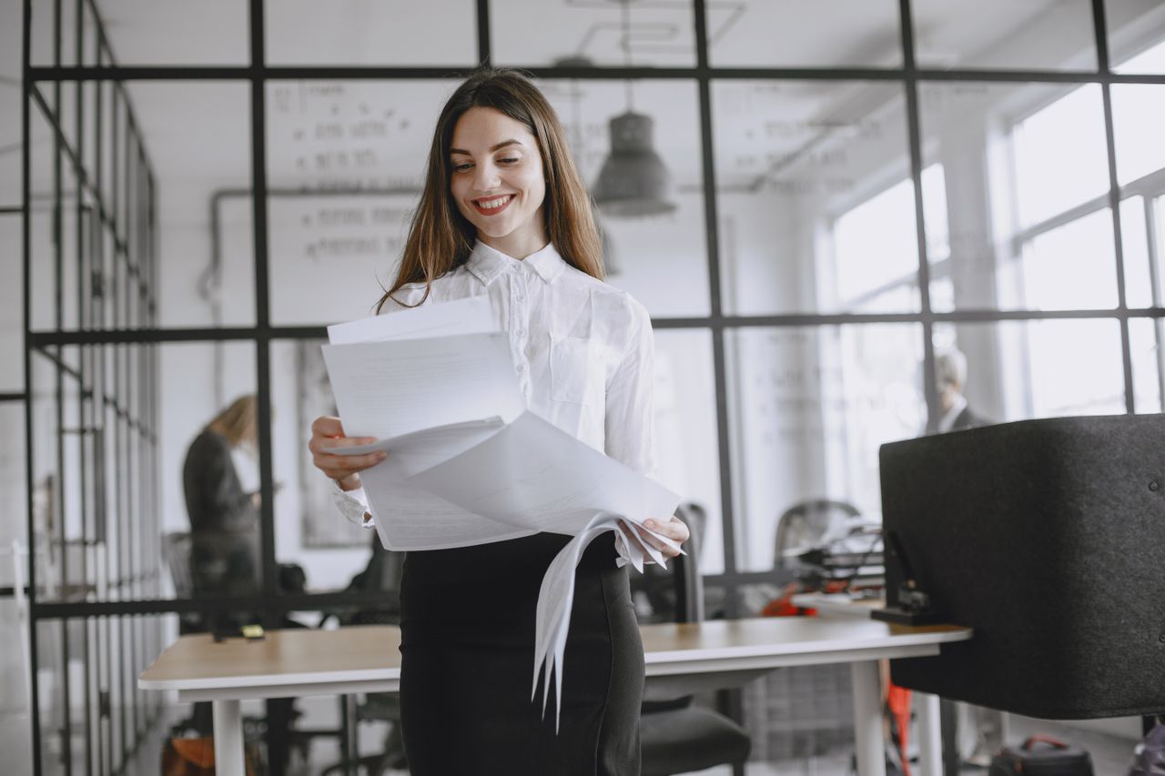 Confident woman with long hair reviewing documents at modern office desk.