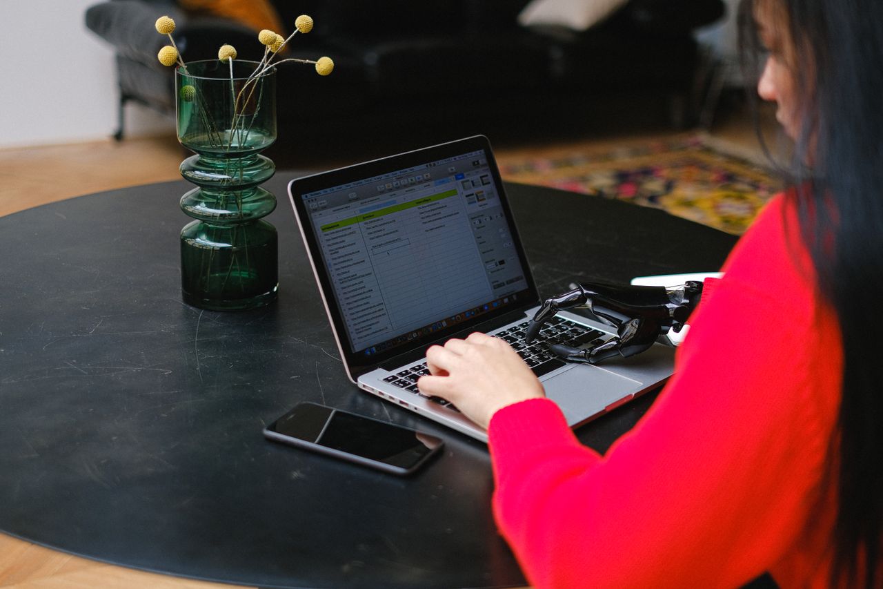 A woman with a prosthetic hand typing on a laptop at a sleek indoor table.