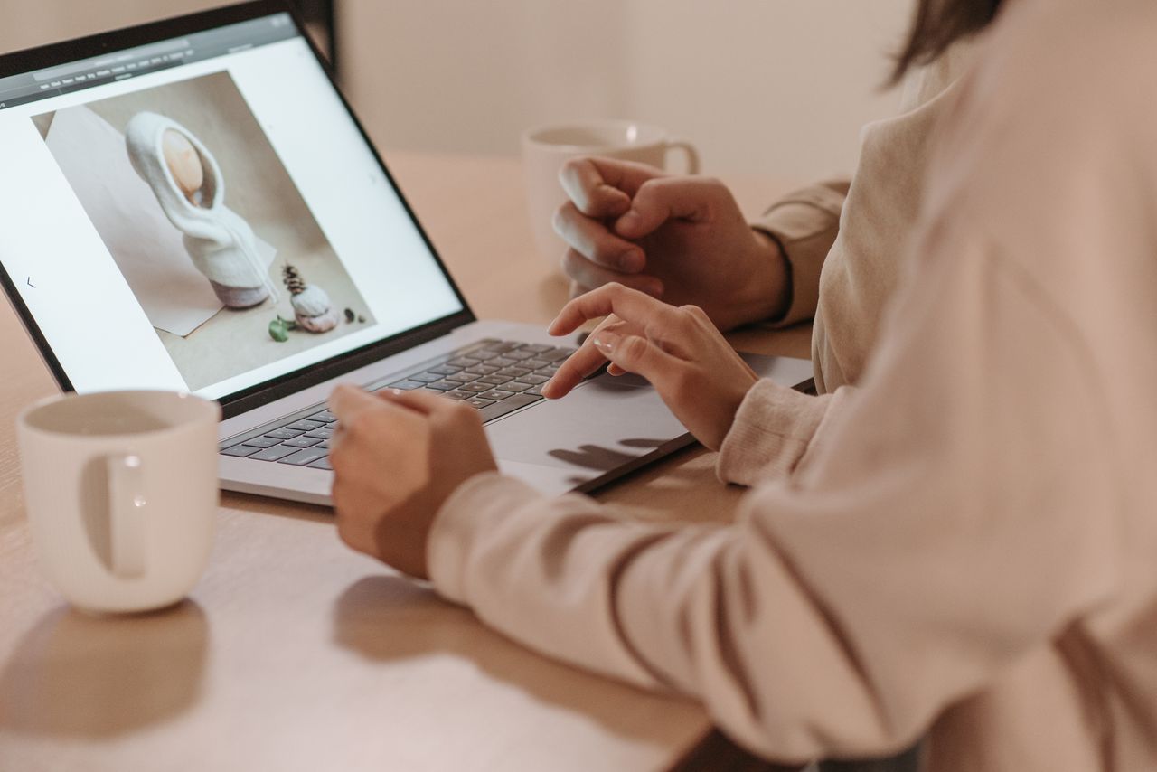 Two individuals reviewing a photo on a laptop, enjoying coffee indoors.