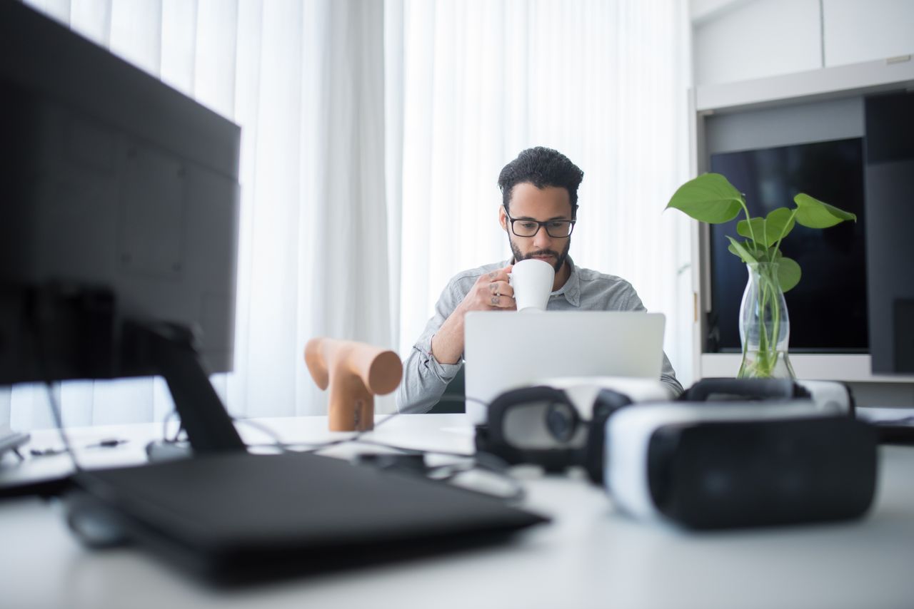 Focused young man sipping coffee while working on laptop in a bright, modern office.